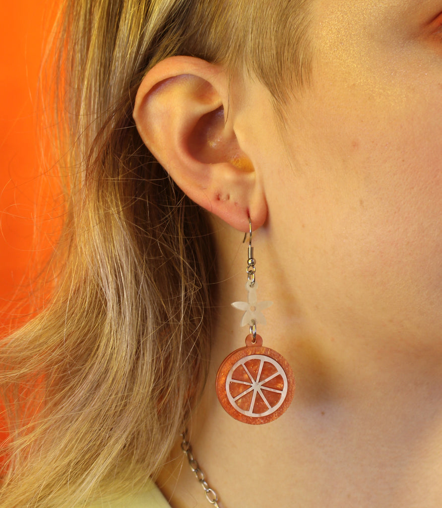 model wearing orange slice pendant suspended from white flower charms on stainless steel earwires