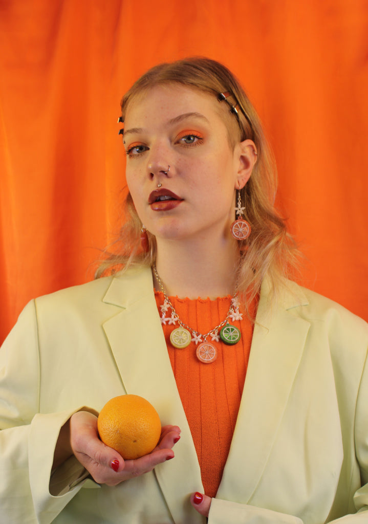 Model wearing necklace featuring lemon, orange and lime slice pendants and white flowers on an oval link stainless steel chain