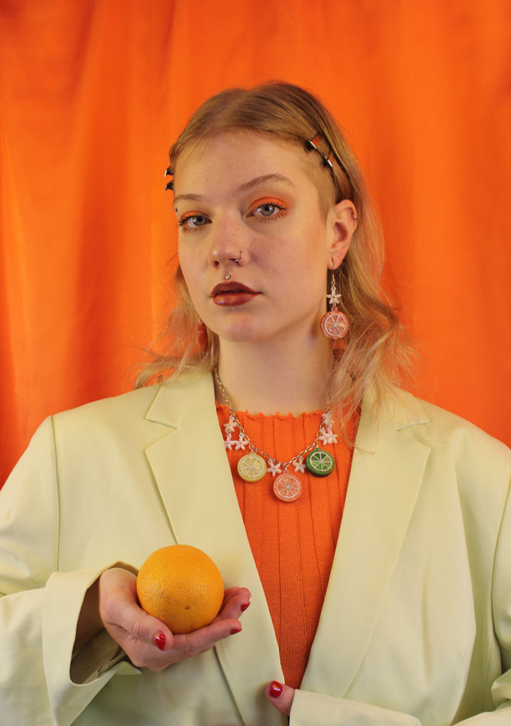 model wearing orange slice pendant suspended from white flower charms on stainless steel earwires