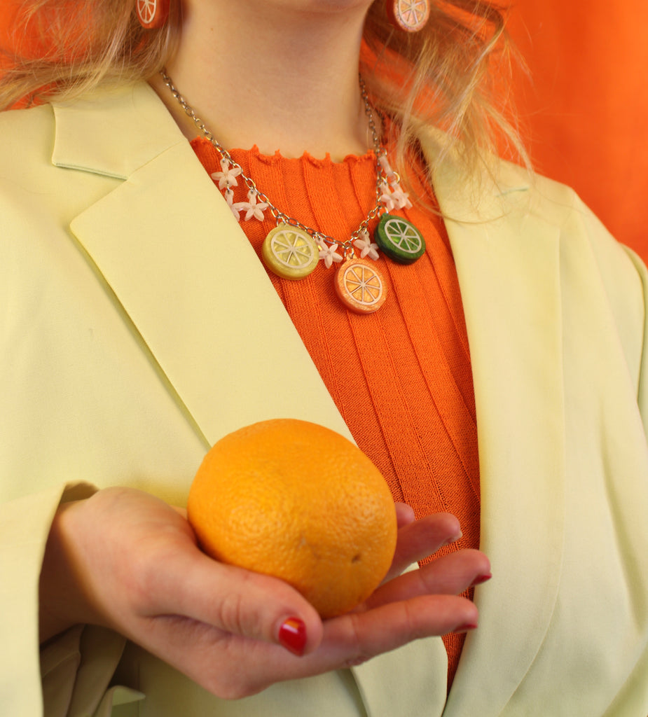 Model wearing necklace featuring lemon, orange and lime slice pendants and white flowers on an oval link stainless steel chain