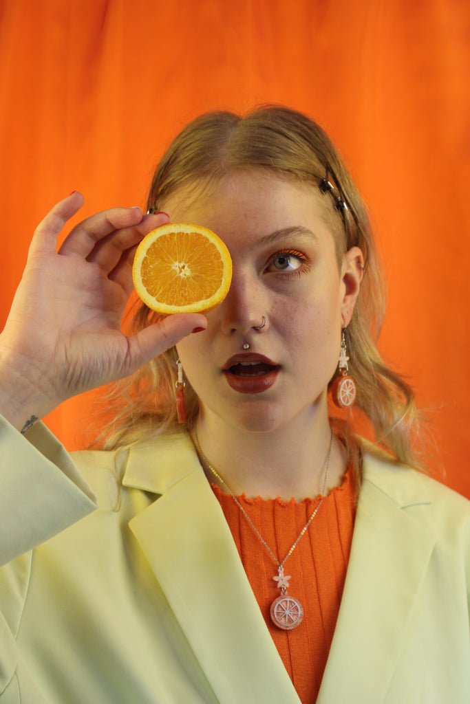 Model wearing Orange slice pendant suspended from a white flower charm on a stainless steel chain