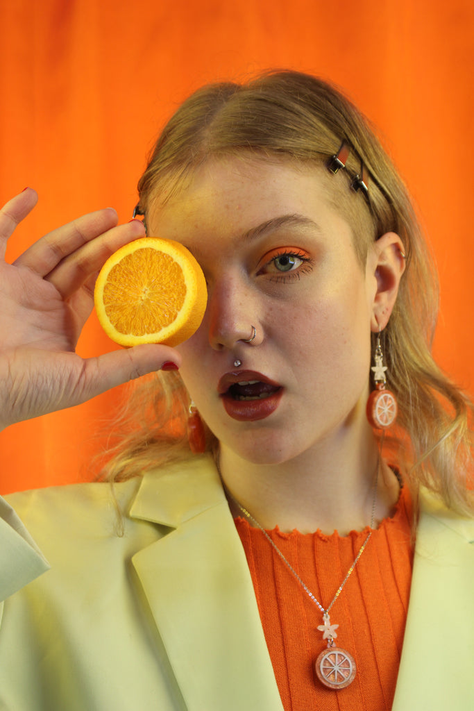 Model wearing Orange slice pendant suspended from a white flower charm on a stainless steel chain