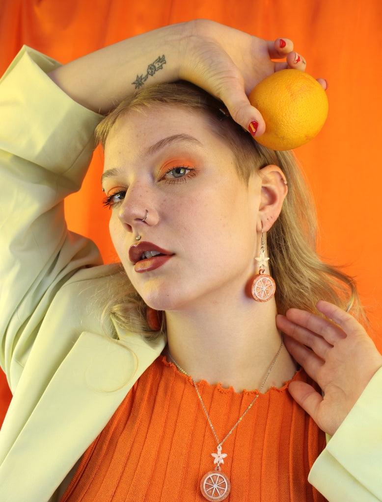 model wearing orange slice pendant suspended from white flower charms on stainless steel earwires