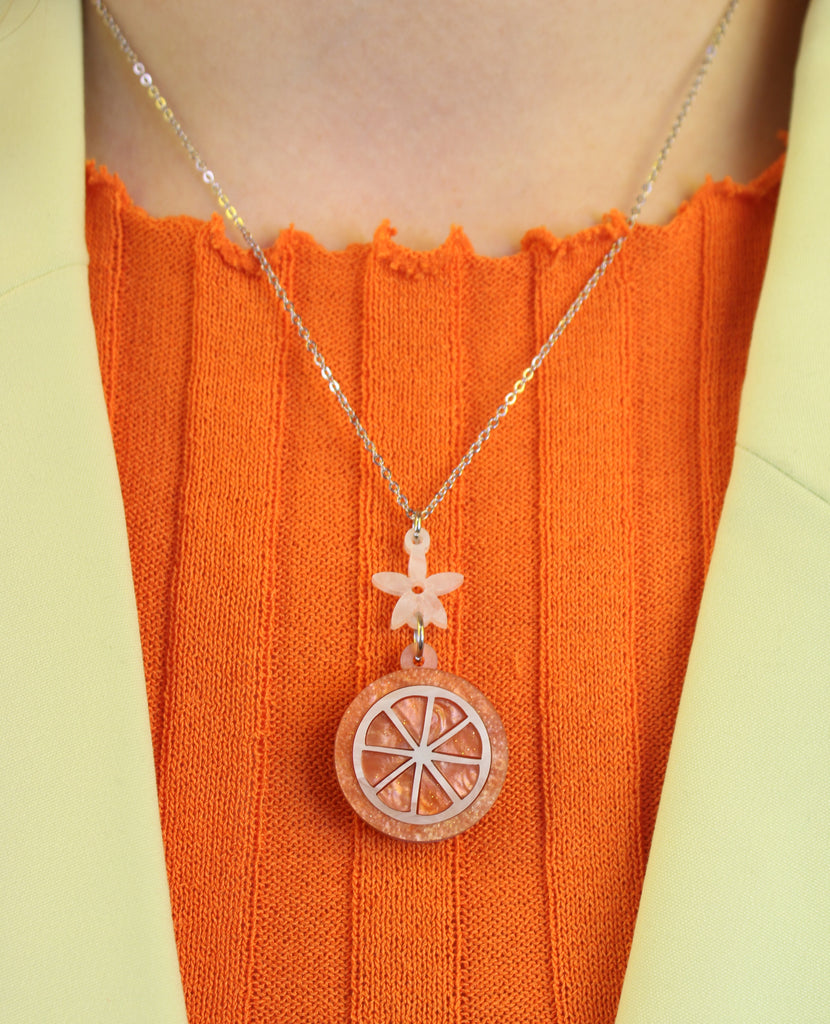 Model wearing Orange slice pendant suspended from a white flower charm on a stainless steel chain