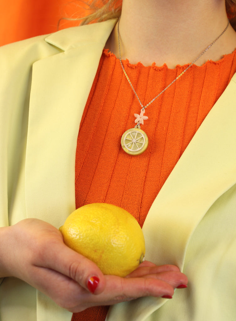 model wearing lemon slice pendant suspended from a white flower charm on a stainless steel chain