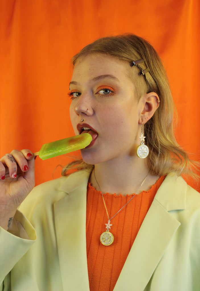 model wearing Lemon slice charms suspended fromn white flower charms on stainless steel earwires