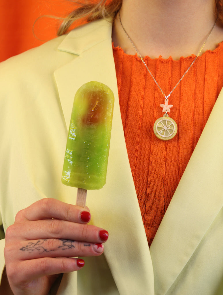 model wearing lemon slice pendant suspended from a white flower charm on a stainless steel chain