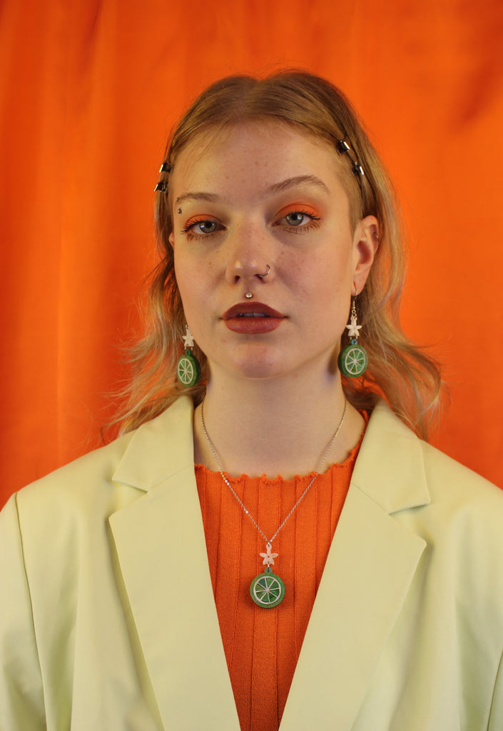 Model wearing Glittery lime fruit slice charm suspended from a white flower on stainless steel earwires