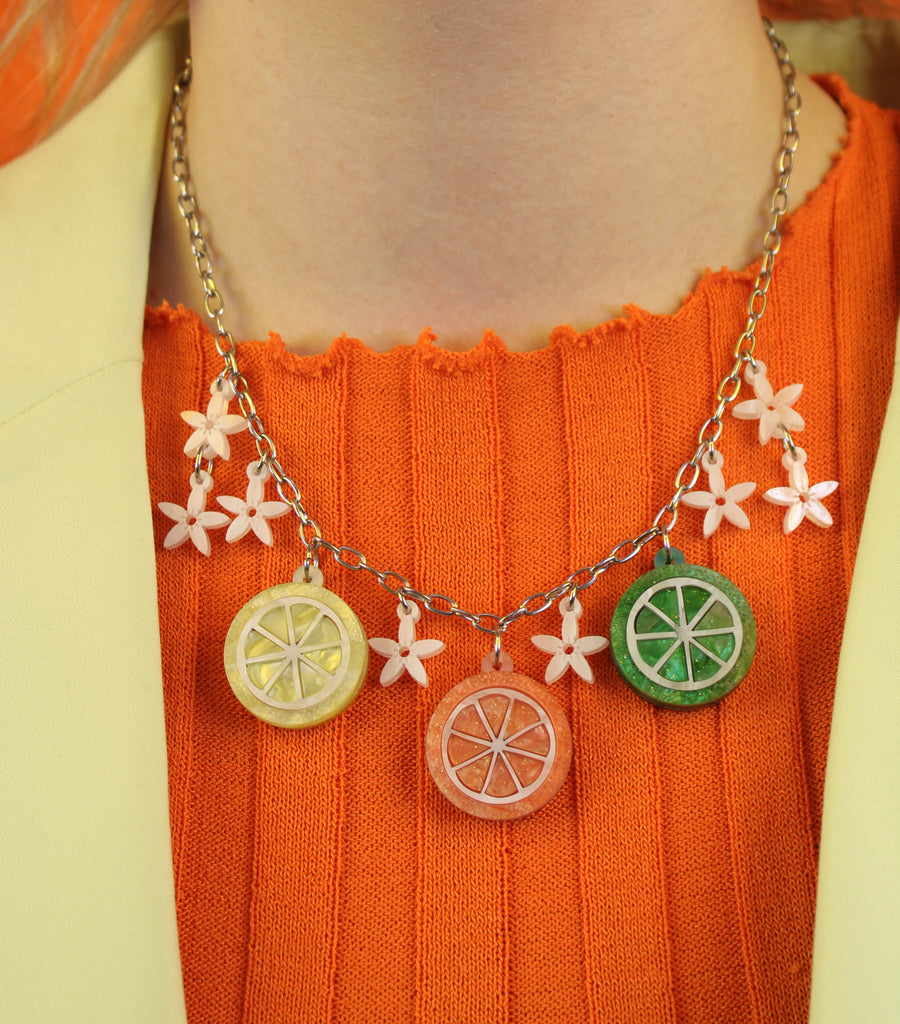 Model wearing necklace featuring lemon, orange and lime slice pendants and white flowers on an oval link stainless steel chain