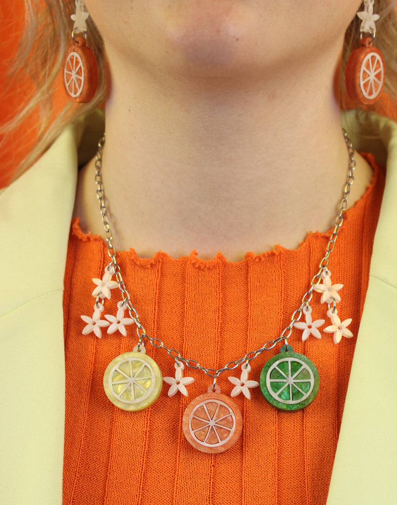 Model wearing necklace featuring lemon, orange and lime slice pendants and white flowers on an oval link stainless steel chain