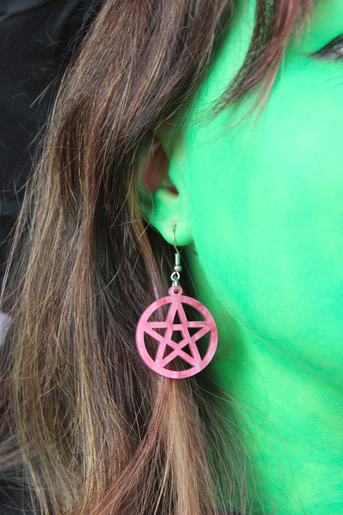 Model wearing marble pink cut out pentacle charms on stainless steel earwires