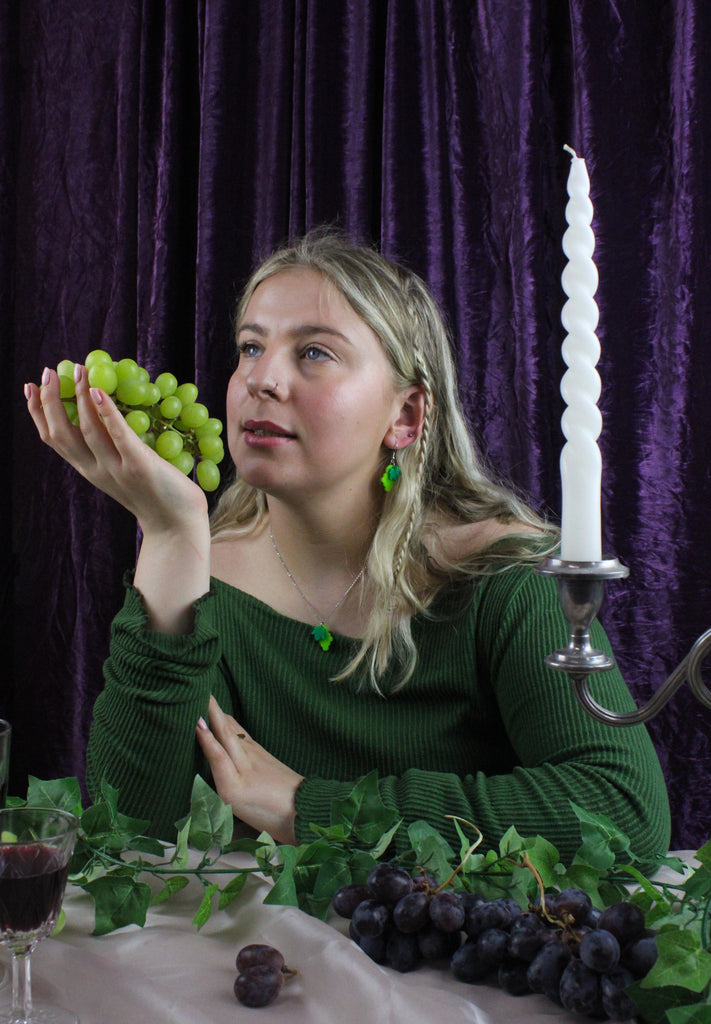 Model wearing Acrylic green grapes charms on stainless steel earwires, holding a bunch of green grapes
