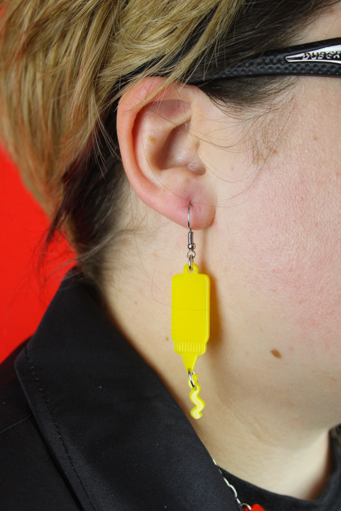 Model wearing Stainless steel earwires featuring mustard acrylic charms with a charm joined to the bottle showing sauce coming out of it