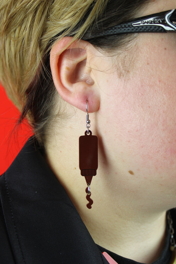 Model wearing Stainless steel earwires featuring barbecue sauce acrylic charms with a charm joined to the bottle showing sauce coming out of it