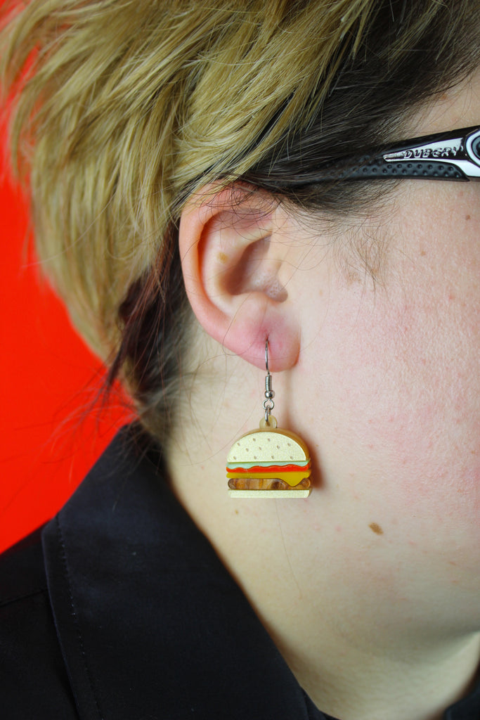 Model wearing Cheeseburger acrylic charms featuring a beige bun and brown marble patty with lettuce and tomato with stainless steel earwires