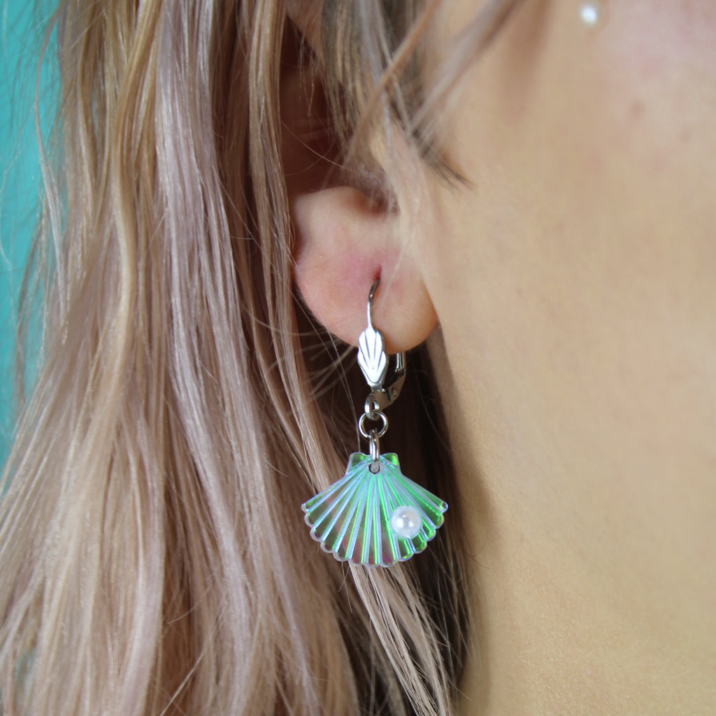 Model wearing Iridescent shell charms featuring a faux pearl on stainless steel hoops