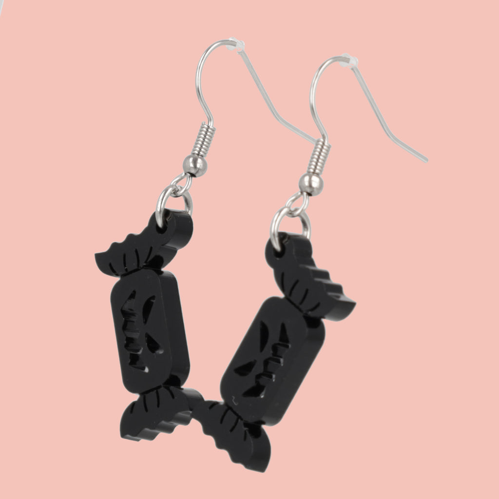 Black sweet wrapper charms with carved out faces on stainless steel earwires