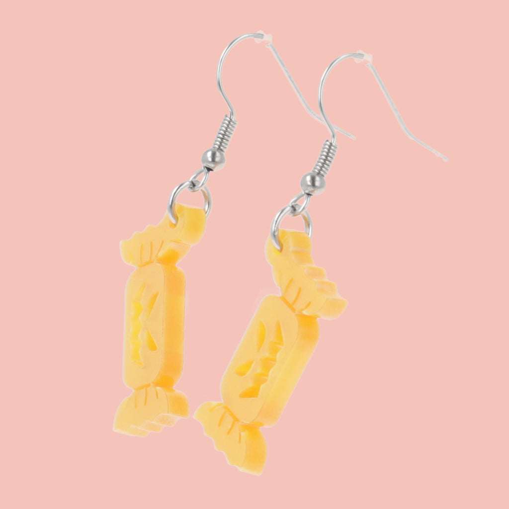 Orange sweet wrapper charms with carved faces on stainless steel earwires