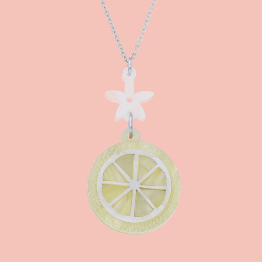 lemon slice pendant suspended from a white flower charm on a stainless steel chain