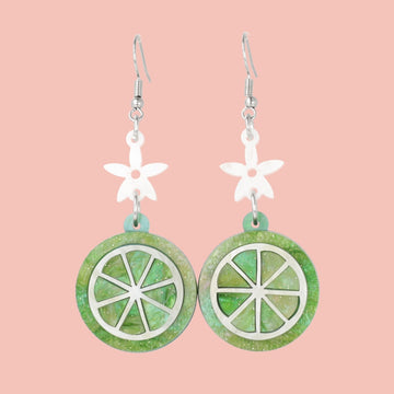 Glittery lime fruit slice charm suspended from a white flower on stainless steel earwires