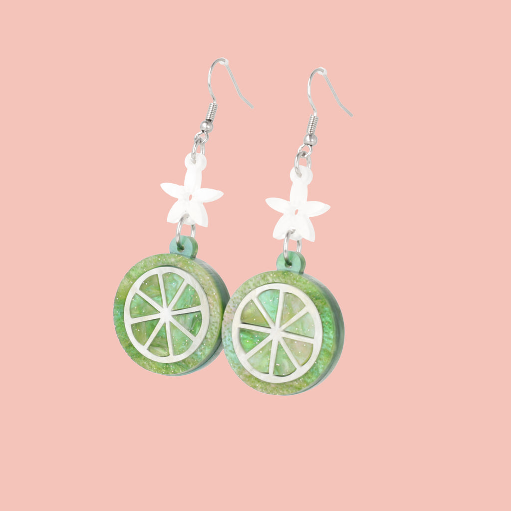 Glittery lime fruit slice charm suspended from a white flower on stainless steel earwires