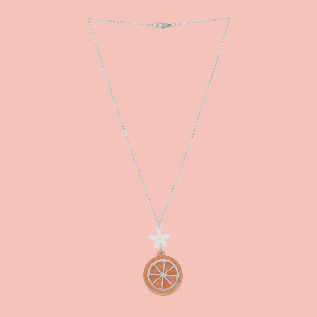 Orange slice pendant suspended from a white flower charm on a stainless steel chain