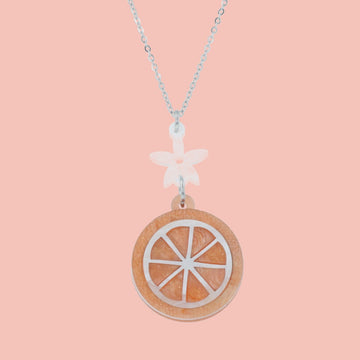 Orange slice pendant suspended from a white flower charm on a stainless steel chain