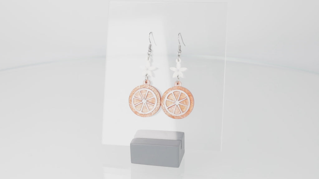 360 view of orange slice pendant suspended from white flower charms on stainless steel earwires