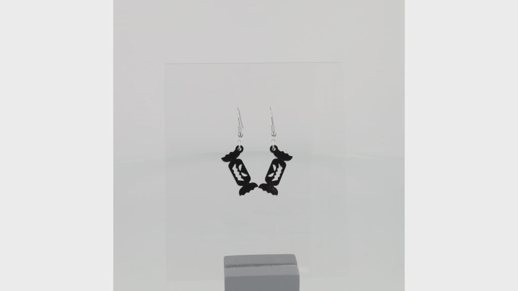 360 view of Black sweet wrapper charms with carved out faces on stainless steel earwires