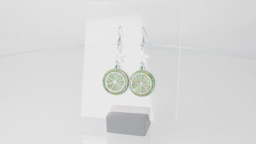 Glittery lime fruit slice charm suspended from a white flower on stainless steel earwires